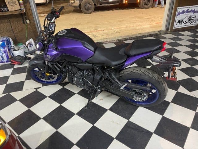 A purple motorcycle is parked on a checkered floor in a garage