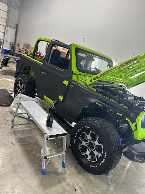 A green jeep is parked in a garage with the hood up