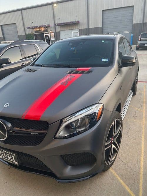 A black car with a red stripe on the hood is parked in a parking lot