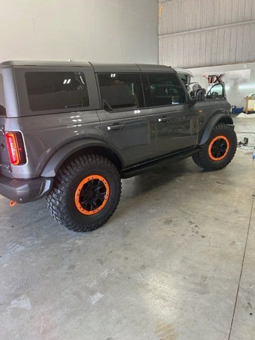 A gray ford bronco with orange wheels is parked in a garage