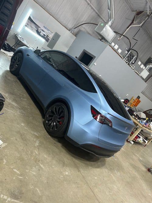 A blue tesla model 3 is parked in a garage