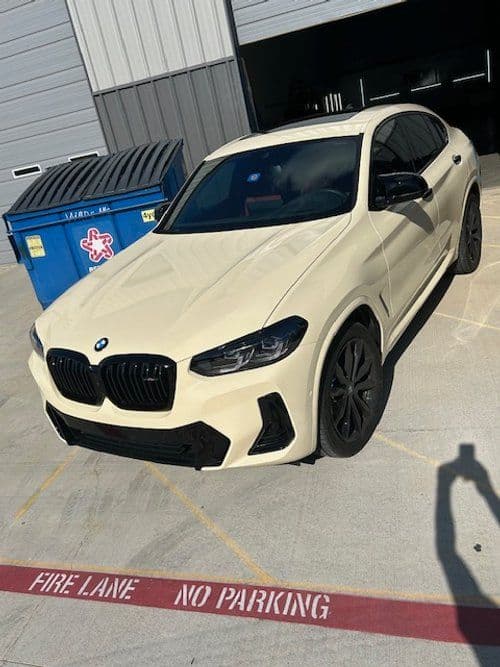 A white bmw is parked in a parking lot next to a dumpster