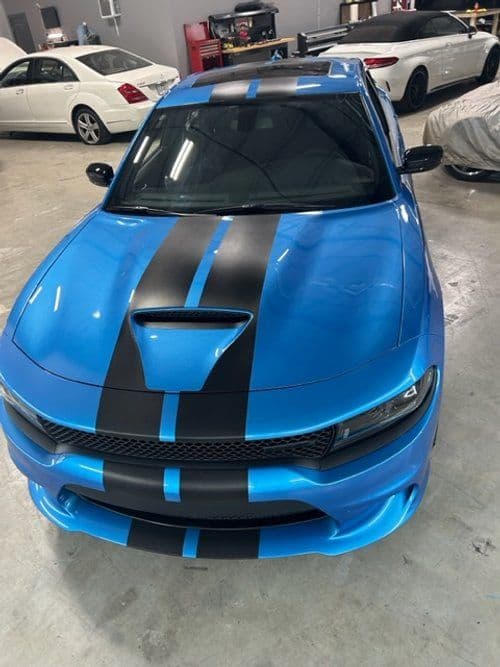 A blue dodge charger with black stripes is parked in a garage