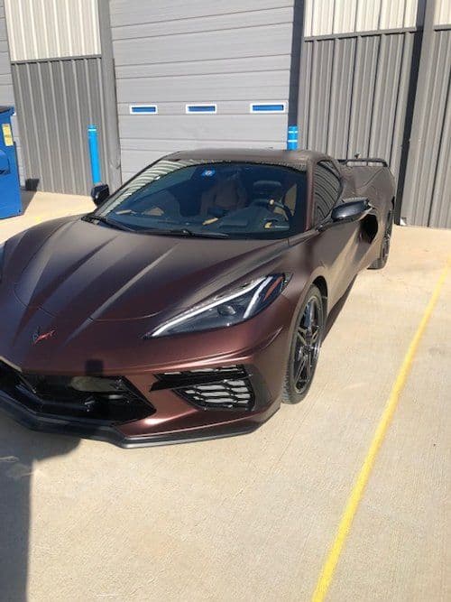 A purple sports car is parked in a parking lot in front of a building