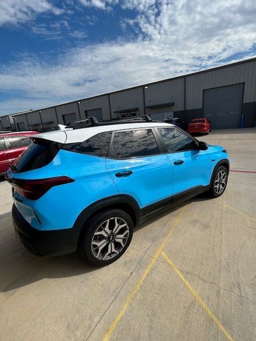 A blue and white car is parked in a parking lot in front of a building