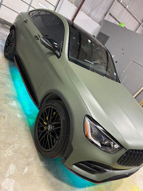 A green car with blue lights underneath it is parked in a garage