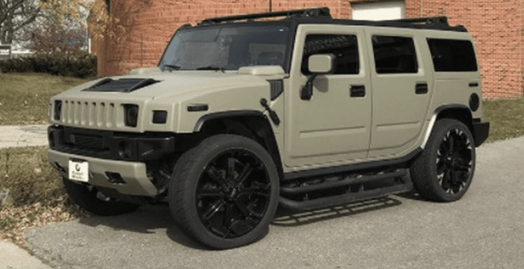 A hummer h2 is parked on the side of the road in front of a brick building