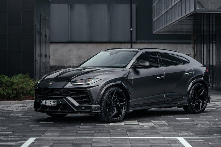 A black lamborghini urus is parked in a parking lot in front of a building